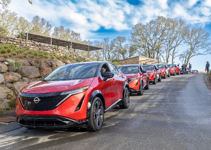 A line of red Nissan EVs parked on a hillside.